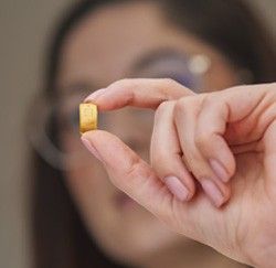 Eine junge Frau zeigt einen 1g Goldbarren zwischen Daumen und Zeigefiinger